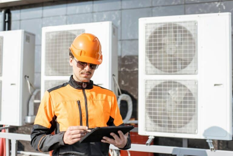 Workman servicing air conditioning or heat pump with digital tablet